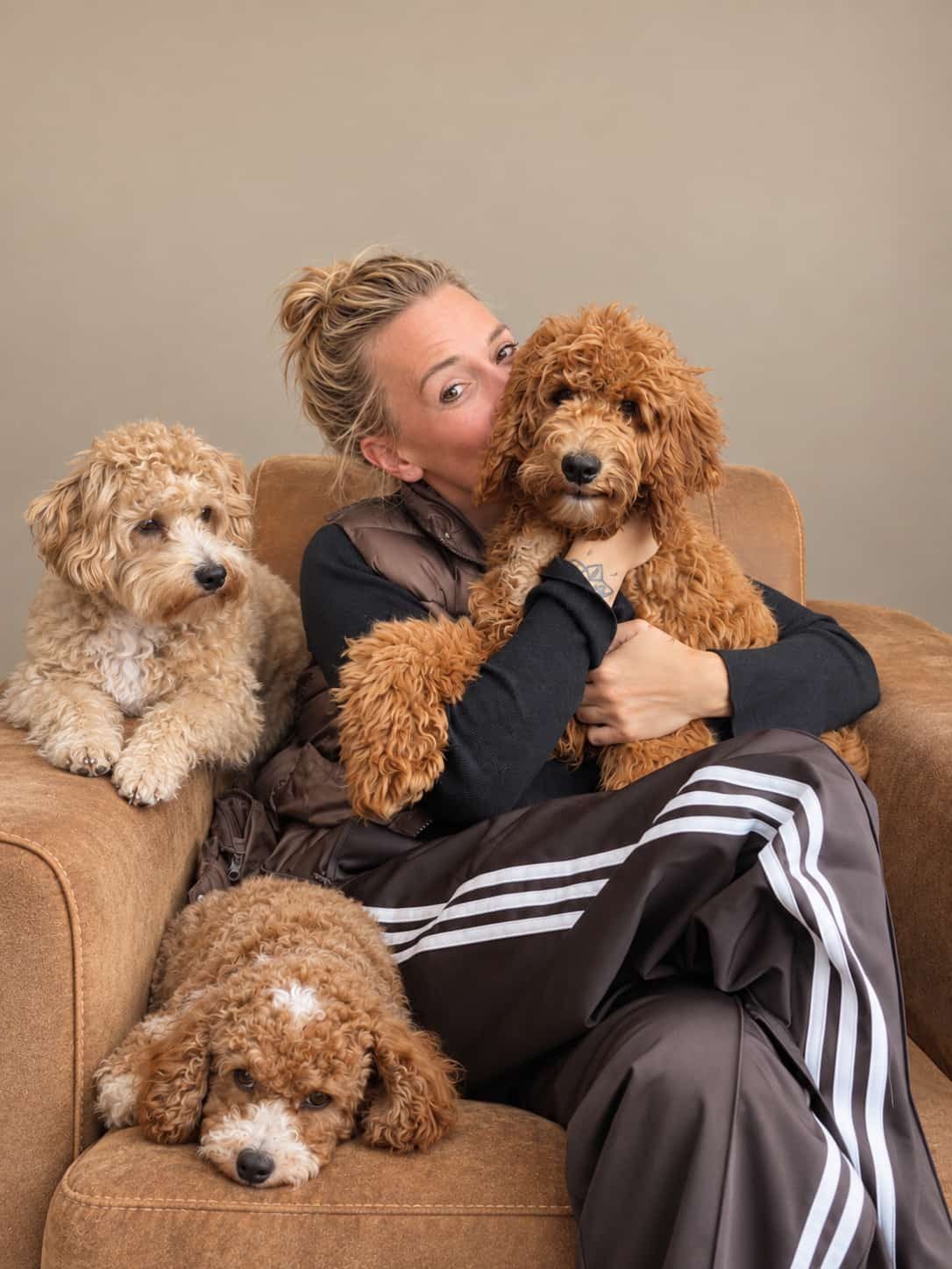 Manon knuffelt een hondje op de bank, met twee hondjes naast haar